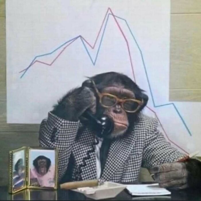 A chimpanzee wearing glasses and a suit, speaking on a vintage phone, with charts in the background, mimicking business attire.