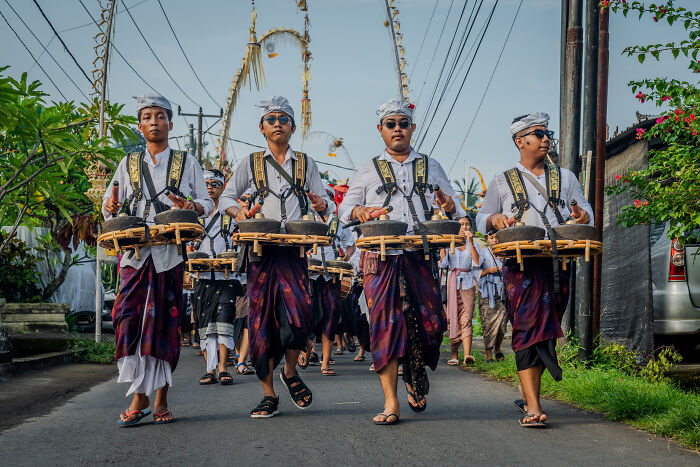 Men in traditional Balinese attire playing drums during Galungan celebration march.