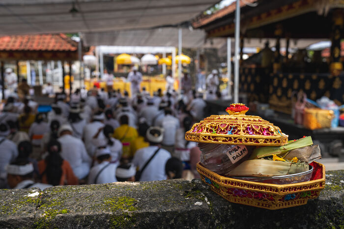 Intricate offerings at a temple during Bali's Galungan celebration with worshippers gathered in the background.