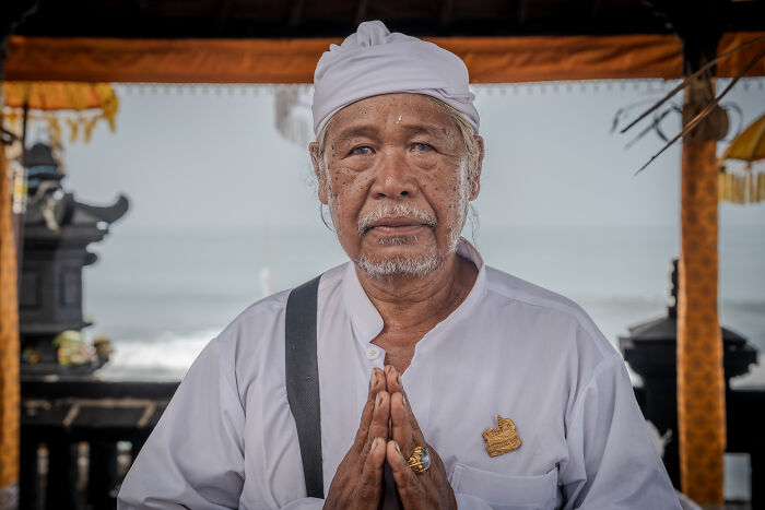 Elderly man in traditional Balinese attire, hands in prayer during Galungan celebration.