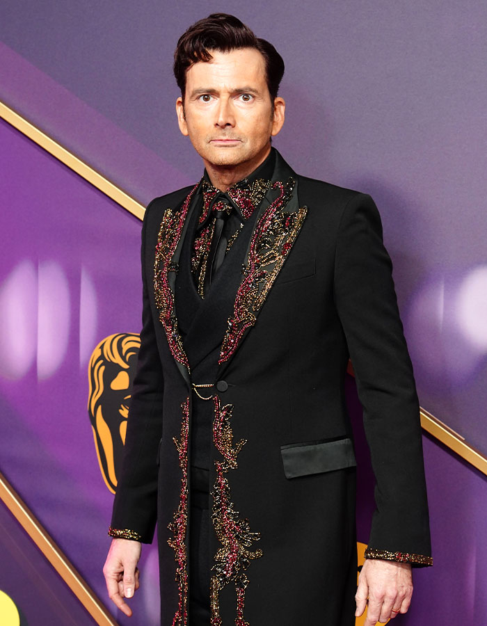 Man in a black suit with gold details on Bafta red carpet showcasing daring outfits.