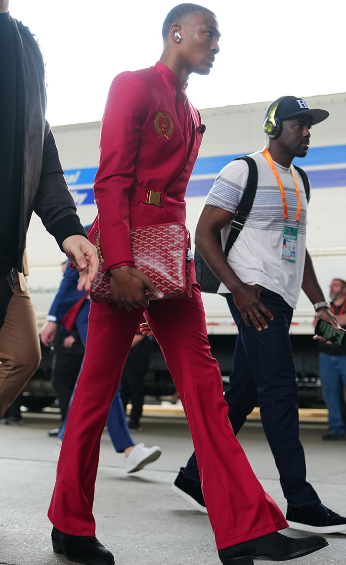 Man in a striking red suit with headphones, holding a matching bag, showcasing a head-turning look at Super Bowl 2025.
