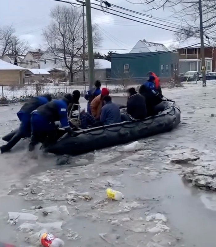 People in a raft on an icy Detroit street after a water main burst, with surrounding ice and debris.