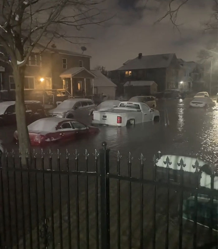 Detroit neighborhood turns icy after water main burst, cars and street covered in water and snow at night.