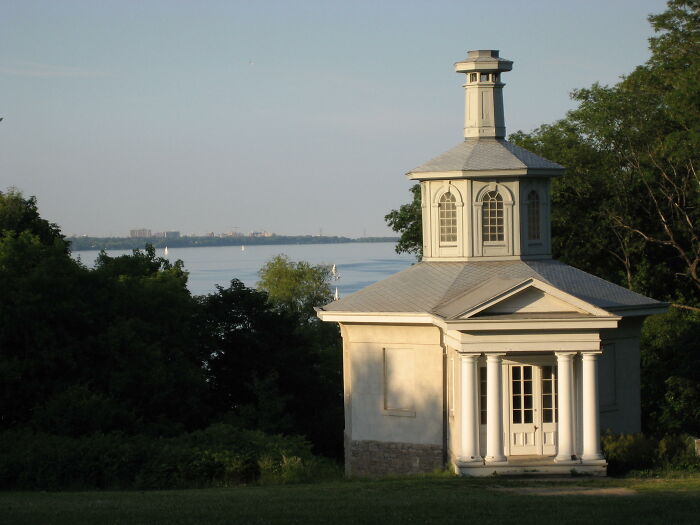 A small, decorative building with columns by a lakeside, representing beautiful useless buildings.