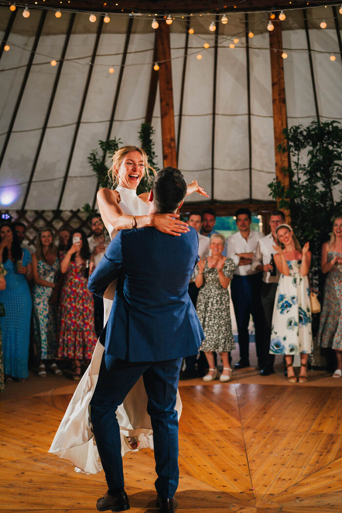 Bride and groom dancing joyfully at a wedding reception, surrounded by smiling guests.