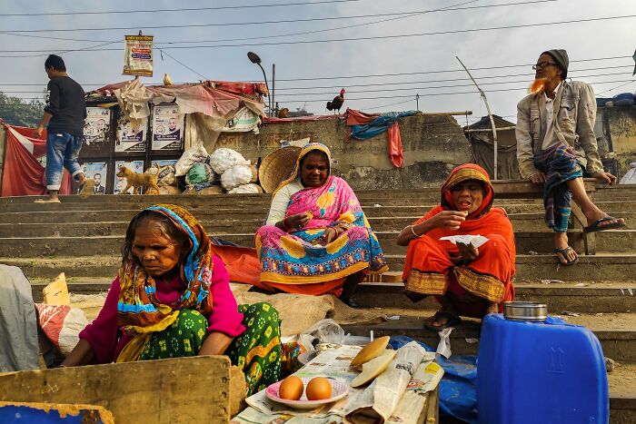 Street photography by Md Enamul Kabir capturing people seated on steps in colorful attire with street market items.