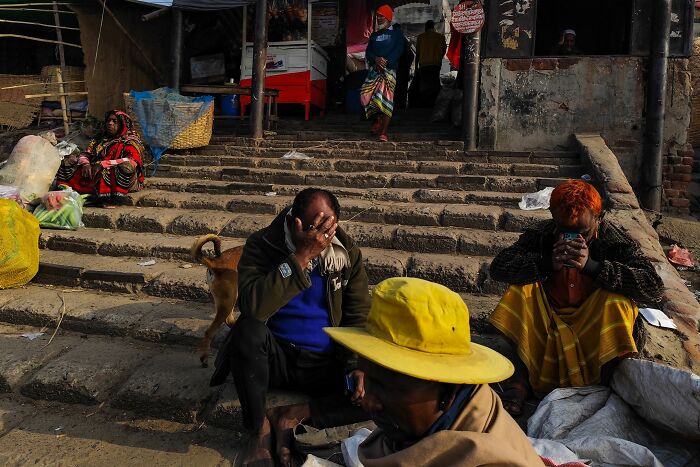 Street photography by Md Enamul Kabir showing people sitting on steps in a busy outdoor market setting.