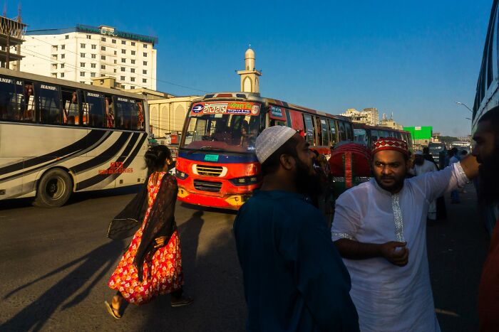Street photography by Md Enamul Kabir capturing daily life with people and buses on a busy city street.