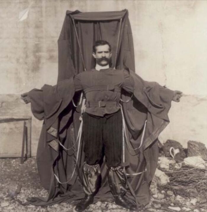 Inventor in flying suit prototype standing against a wall, showcasing early aviation creativity and design.