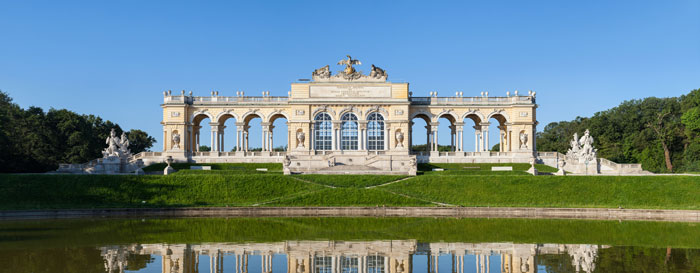 Beautiful facade of a historical building reflected in a pond on a sunny day, showcasing architecture.