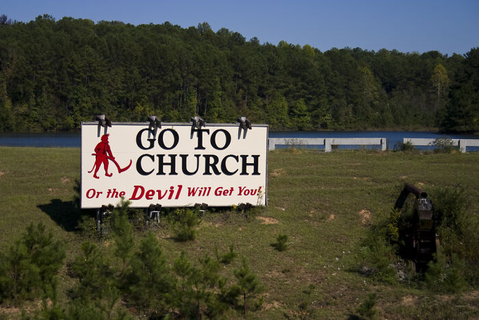 Billboard in a rural area reading "Go to church or the devil will get you," showcasing culture shock in the countryside.