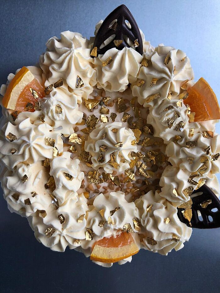 Luxurious dessert topped with gold flakes, cream swirls, chocolate, and orange slices showcasing fascinating culinary art.