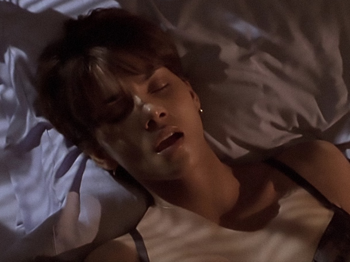Halle Berry in bed scene without prosthetics, wearing a tank top, with a relaxed expression, lit by soft ambient lighting.