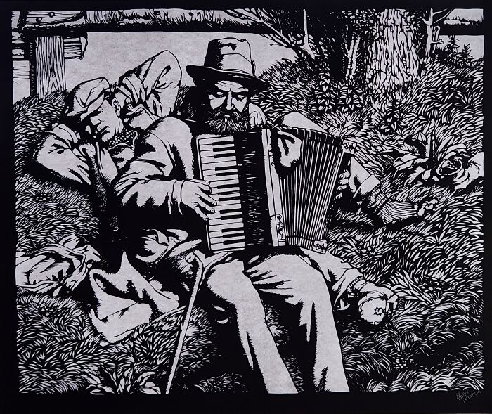 Paper artwork hand-cut with a scalpel showing a man playing an accordion beside a resting figure in a forest setting.