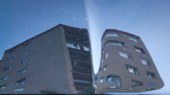 Distorted reflection of Hungary's panel buildings on a glass surface under a clear blue sky.