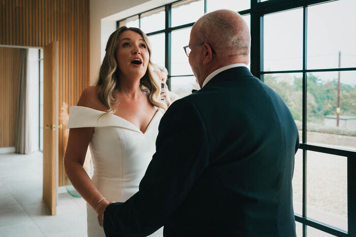 Bride and father share an emotional moment at a wedding by a large window, highlighting wedding photography.