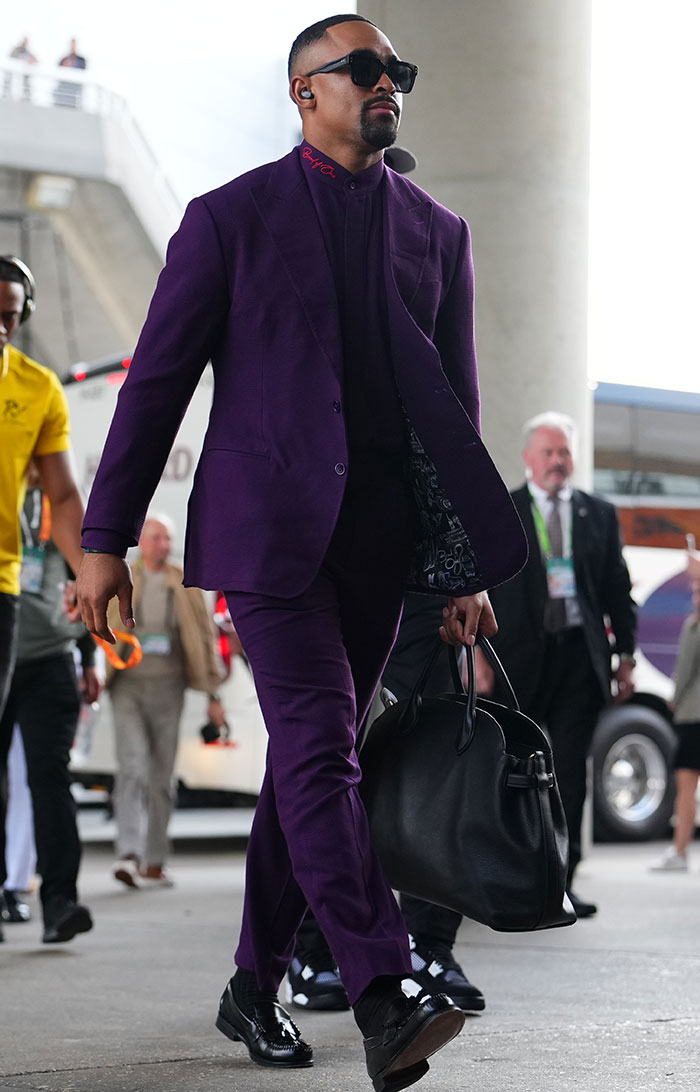 Man in a purple suit with sunglasses and a black bag, showcasing a bizarre look at Super Bowl 2025.
