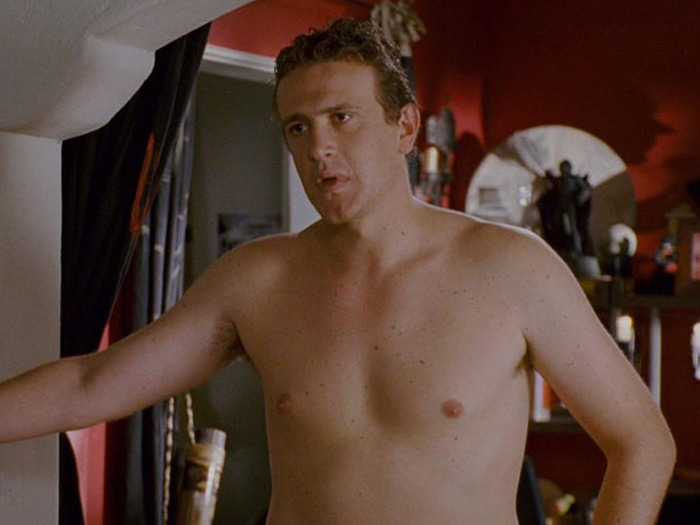 Jason Segel in a room, shirtless, refusing prosthetics, with a red wall and various objects in the background.