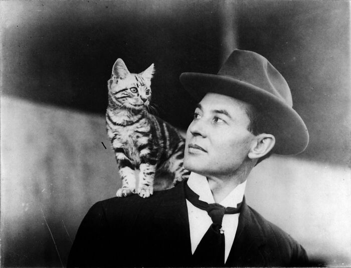 Vintage photo of a man in a suit with a cat on his shoulder, both looking to the right.