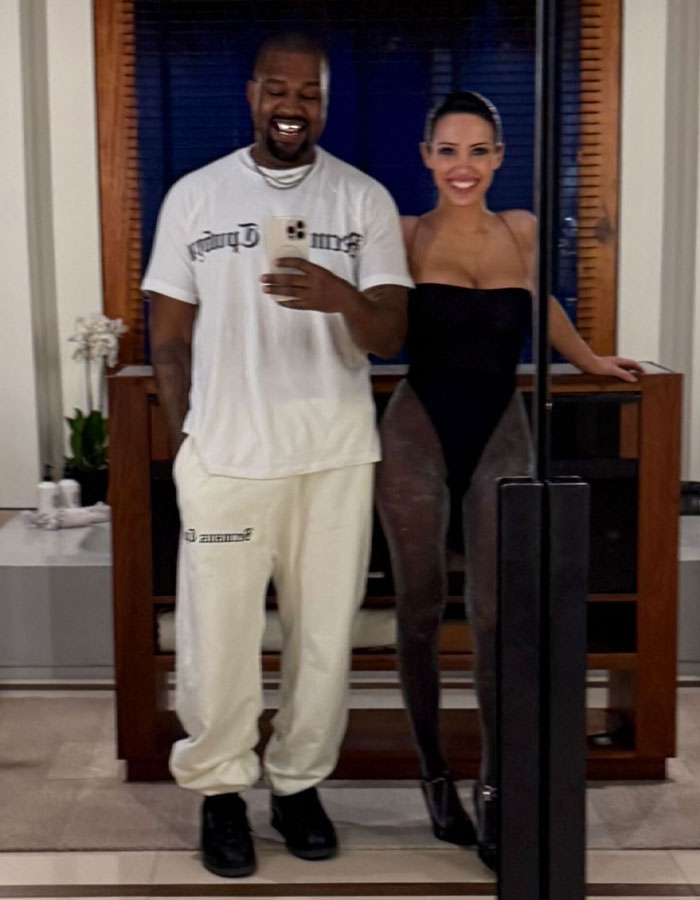 Man in white shirt taking a selfie with a woman in a black outfit, smiling indoors, related to Kanye West Super Bowl ad.
