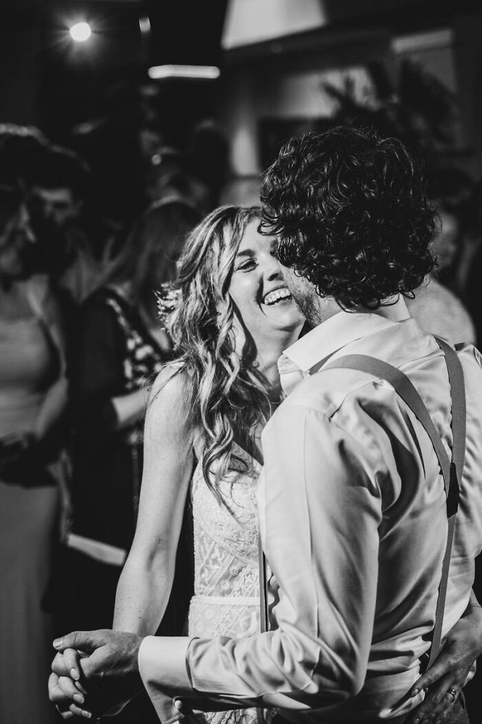 Black and white photo of a couple laughing and dancing closely at a wedding celebration.
