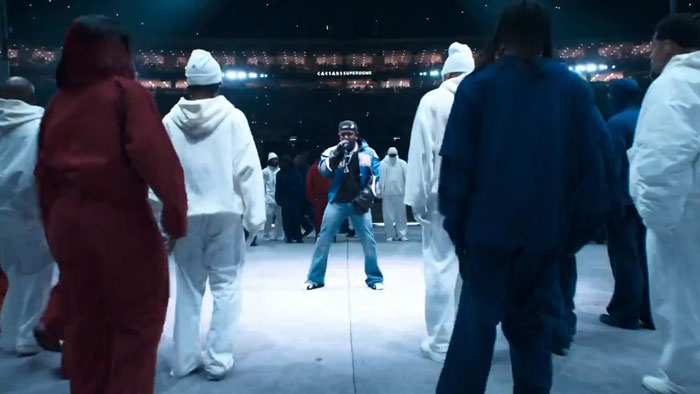 Kendrick Lamar performs at halftime show with a group of dancers in various colored outfits. Kendrick Lamar performs at halftime show with a group of dancers in various colored outfits.
