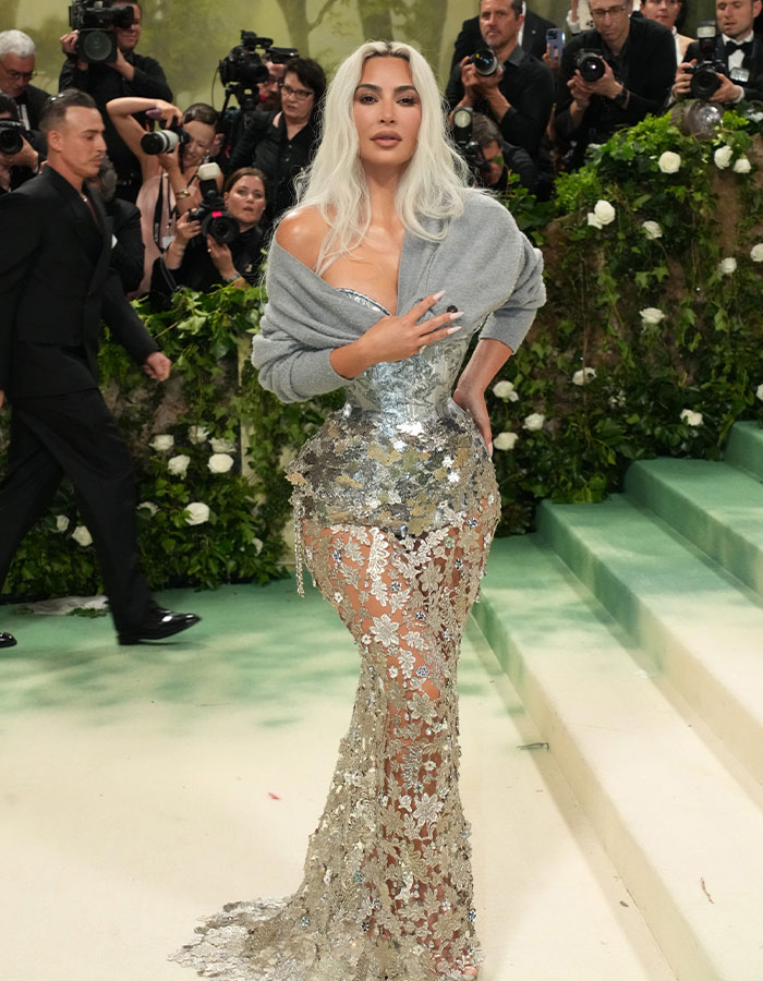 Kim Kardashian at the Met Gala in a tight, shimmering corset dress, surrounded by photographers.