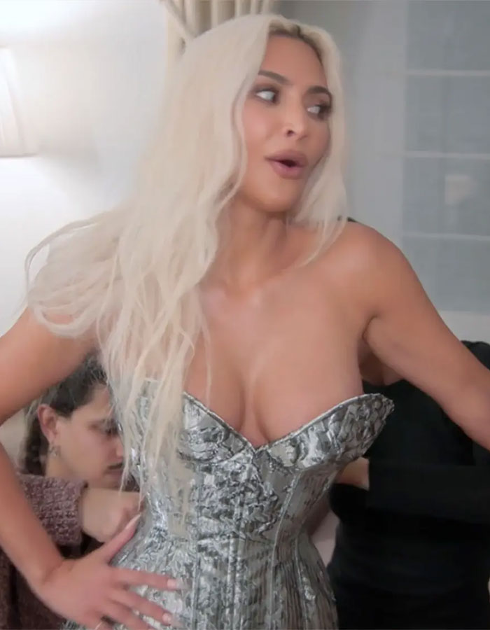 Woman in a silver corset, styled with long blonde hair.