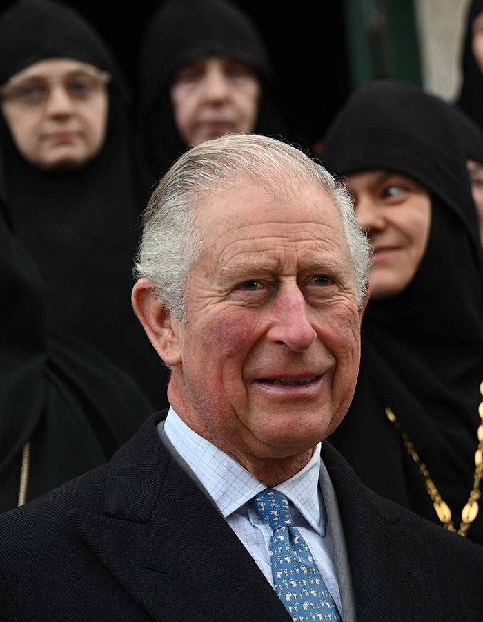 King Charles in a formal suit, surrounded by people in black attire, amid royal crisis discussions.
