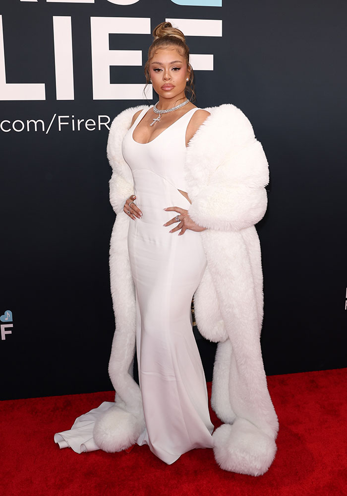 Outfit at the 67th Grammy Awards red carpet: woman in a fitted white gown with fur accessories, posing confidently.