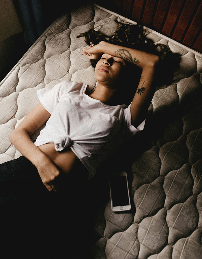 Woman lying on a mattress, phone nearby, reflecting period tracker debate in mobile game context.