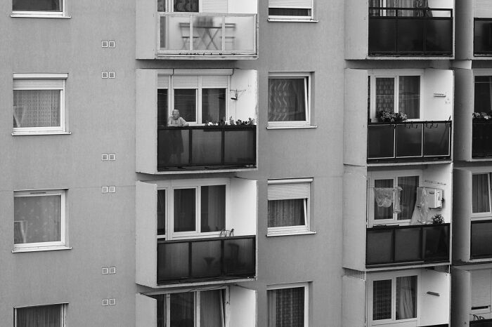 Black and white photo of Hungary's panel buildings with balconies and windows, featuring a person on one balcony.