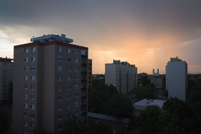 Hungary’s panel buildings at sunset with trees below and a dramatic sky above.