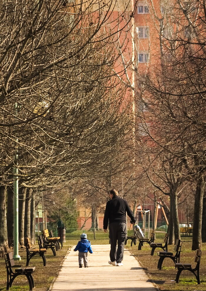 Father and child walking in a park with Hungary's panel building in the background.