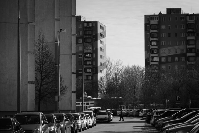 Hungary’s panel buildings in black and white, with parked cars lining the street and a pedestrian walking.