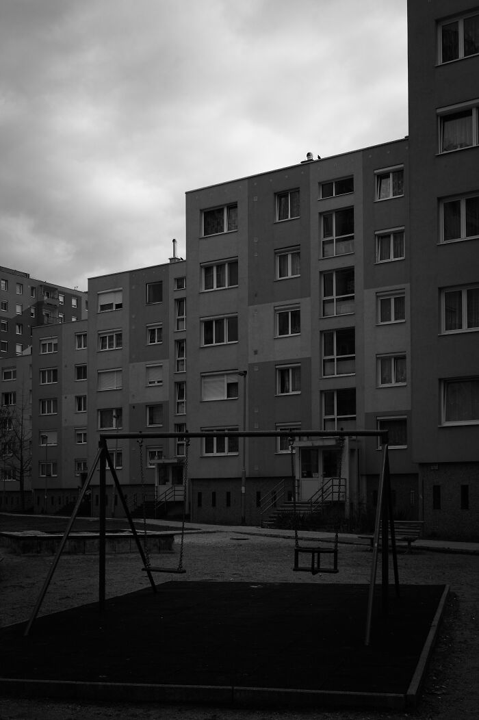 Hungary's panel buildings in a monochrome photo with a playground in the foreground under a cloudy sky.