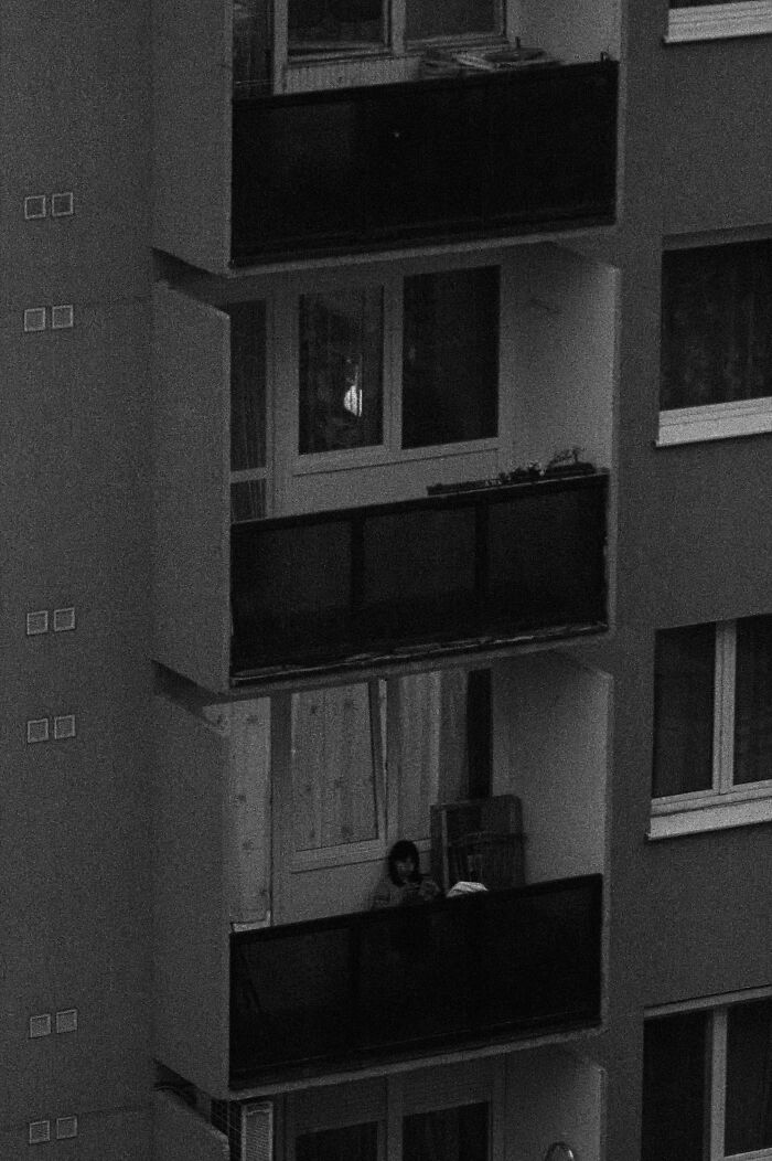 Hungary's panel buildings with a lone person sitting on a balcony in a monochrome setting.