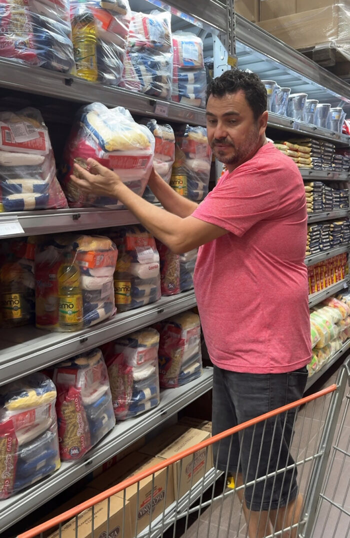 Man in a pink shirt selecting dog food from a store shelf, dedicated to feeding stray dogs for 25 years. Man in a pink shirt selecting dog food from a store shelf, dedicated to feeding stray dogs for 25 years.