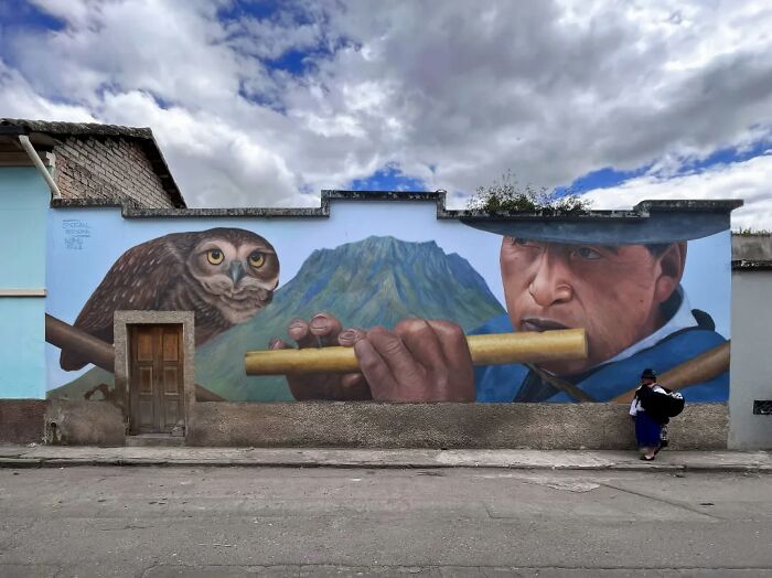Chilean artist's mural of a man playing a flute and an owl against a mountain backdrop.
