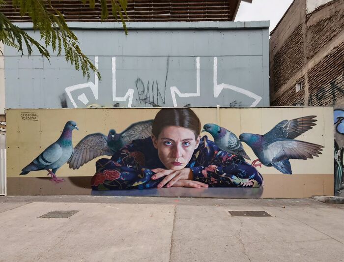 Chilean artist's mural of a woman with pigeons, vibrant and detailed on an urban wall.