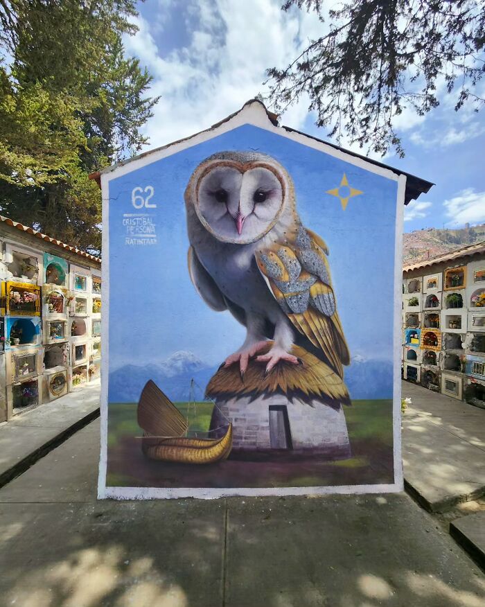 Mural by Chilean artist depicting a large, realistic owl perched on a roof with a small boat beside it, under a clear sky.