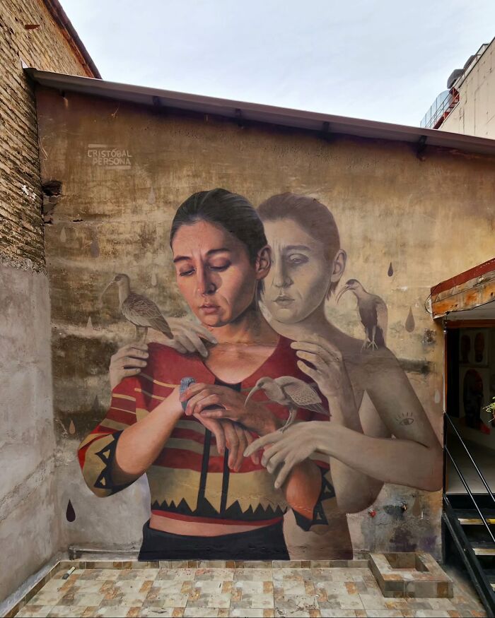 Chilean artist's mural depicting a woman with birds on her hands and a faded figure embracing her.
