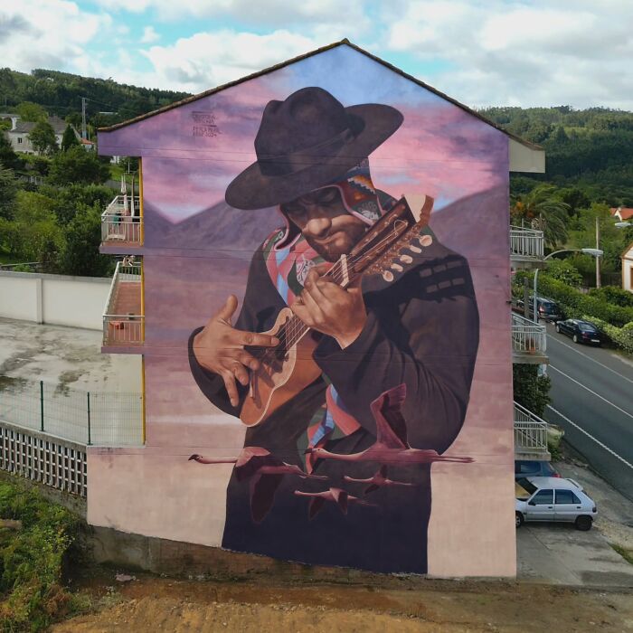 Chilean artist's mural of a musician with a hat, painted on a building, under a vibrant sky.