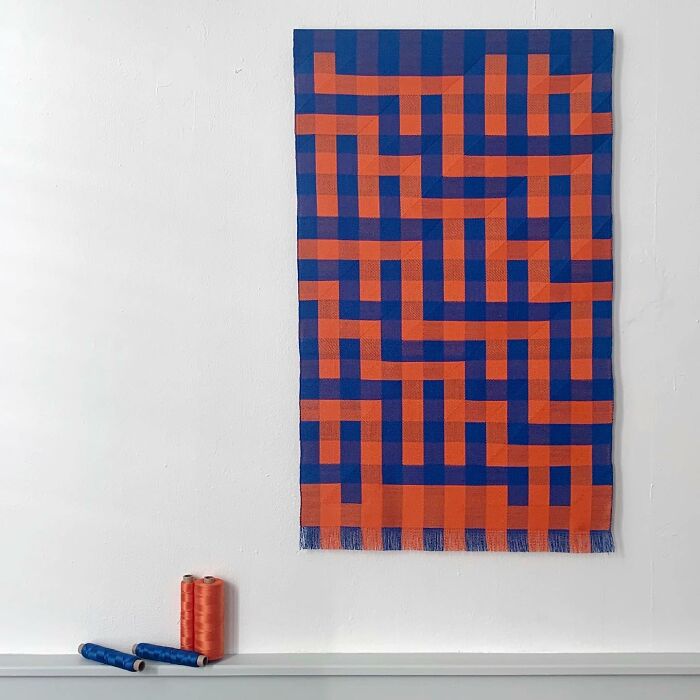 Intricate geometric weave art with blue and orange patterns creating optical illusions, alongside spools of thread.