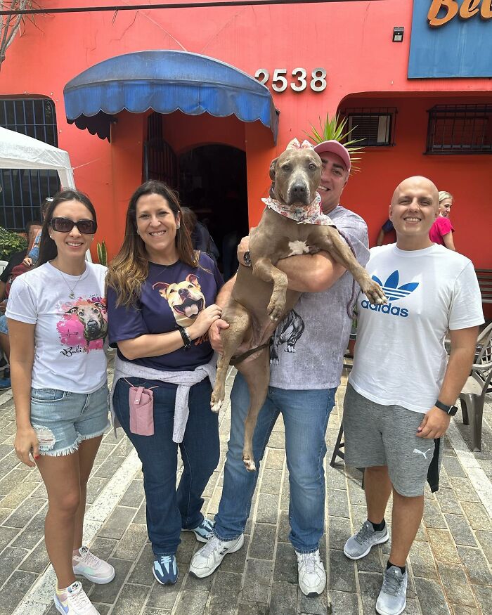 Group of people smiling with a rescued Pit Bull dog outside an orange building. Group of people smiling with a rescued Pit Bull dog outside an orange building.