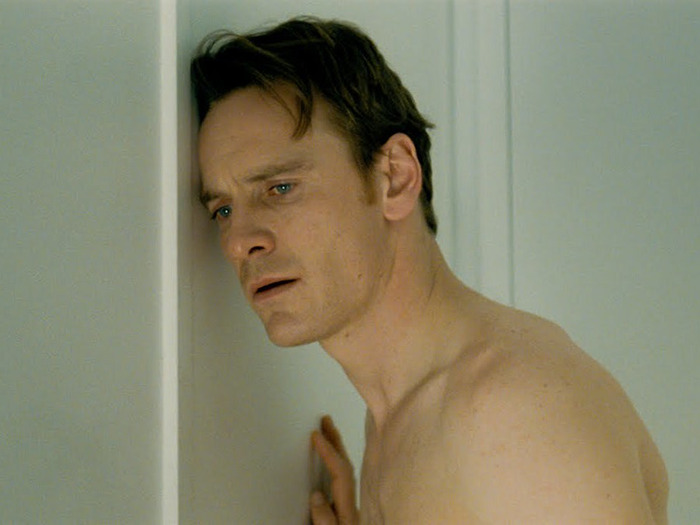 Michael Fassbender in an intense scene, demonstrating a refusal to use prosthetics, standing shirtless against a wall.