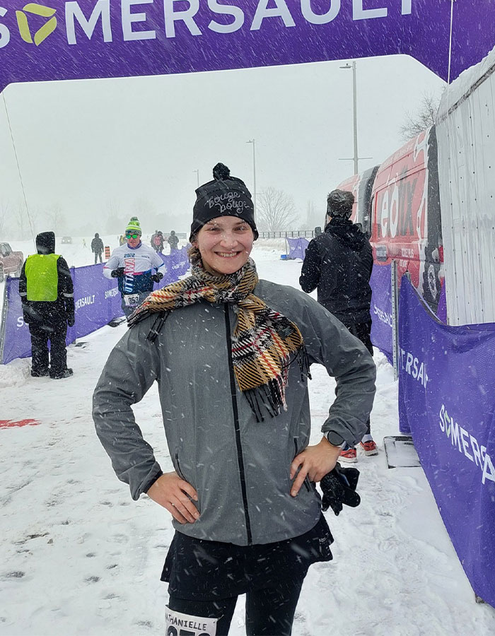 Trans runner standing confidently in snowy race finish area, promoting inclusion in women's sports.