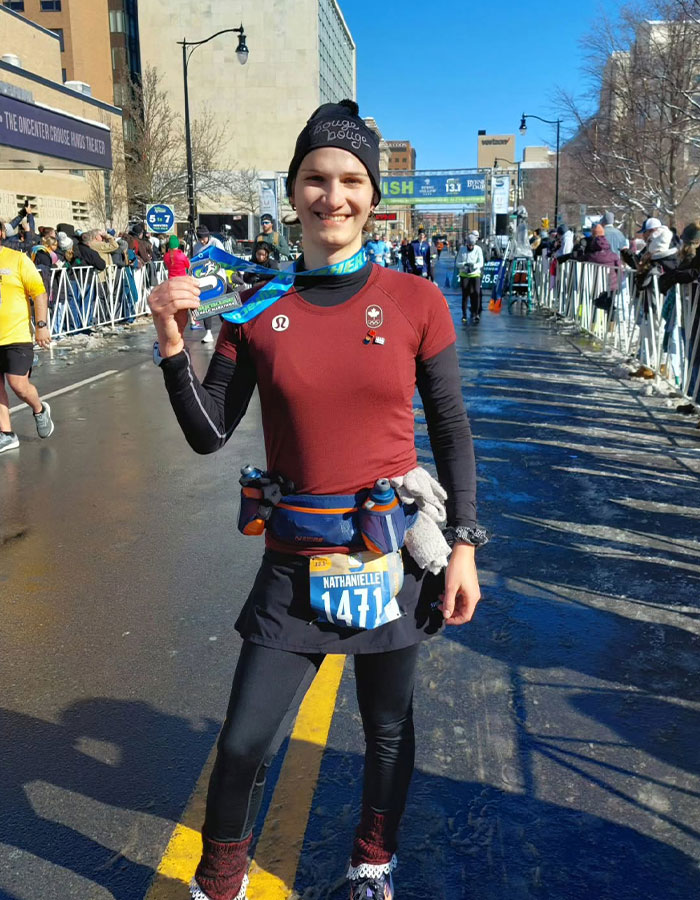 Runner holding a medal, wearing a race bib, advocating for transgender inclusion in women's sports at the finish line.