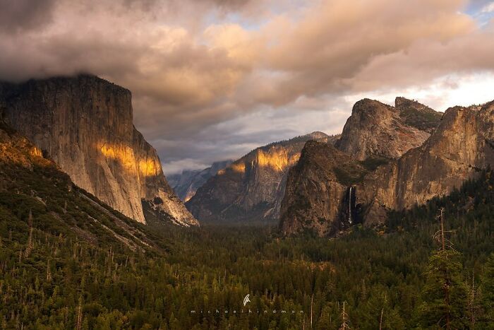 Intimate landscape showcasing dramatic mountain textures at sunset, with lush forests and cloudy skies.